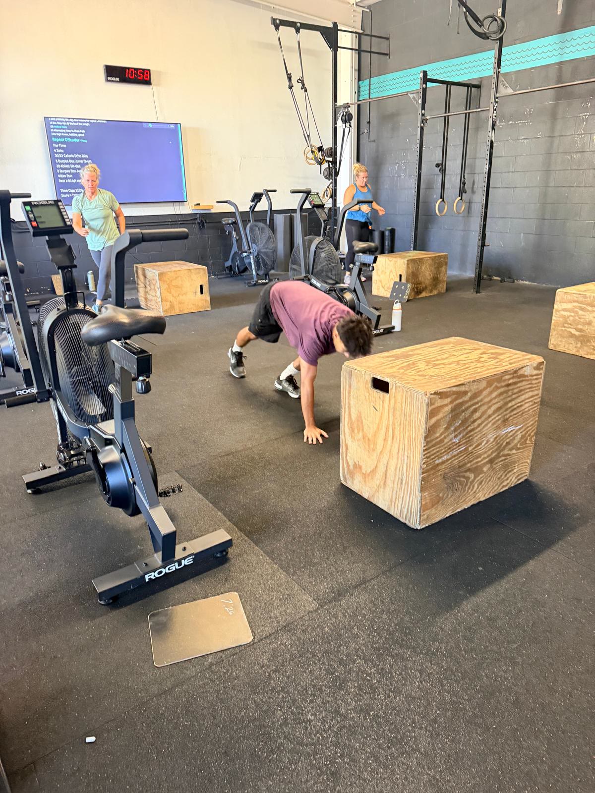 Athlete doing burpee next to wooden box, others training behind